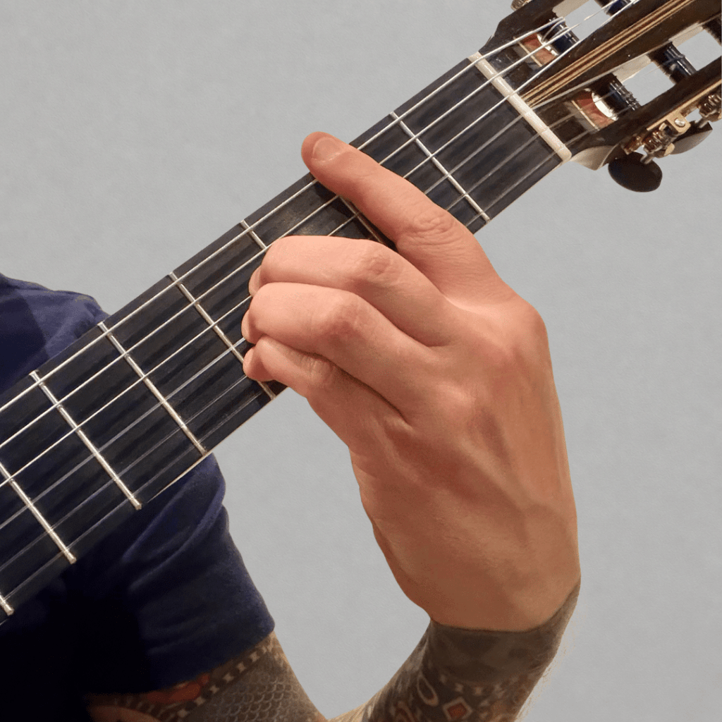 hand playing the B major chord shape on classical guitar with full barre